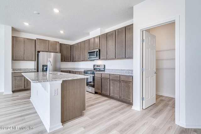 kitchen featuring appliances with stainless steel finishes, light wood-type flooring, light stone countertops, and a center island with sink