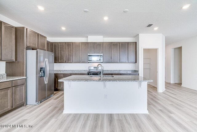 kitchen with stainless steel appliances, a sink, visible vents, light stone countertops, and a kitchen bar