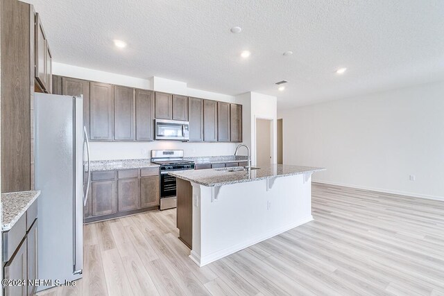 kitchen featuring appliances with stainless steel finishes, light hardwood / wood-style flooring, a center island with sink, sink, and light stone counters