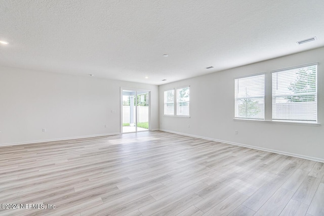 empty room with light wood-type flooring, a textured ceiling, and baseboards