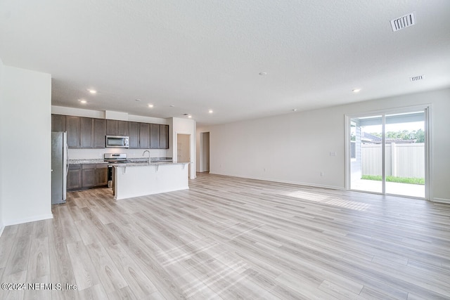 unfurnished living room featuring light hardwood / wood-style floors, sink, and a textured ceiling