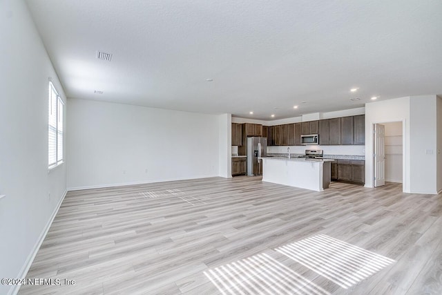 kitchen featuring appliances with stainless steel finishes, open floor plan, a kitchen island with sink, light countertops, and light wood-type flooring