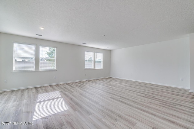 empty room with light wood-style flooring, a textured ceiling, visible vents, and baseboards