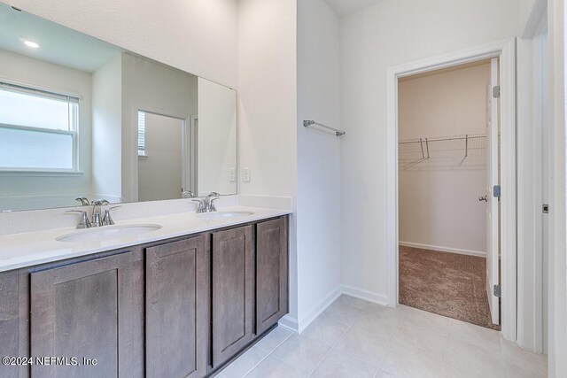 full bathroom with double vanity, a spacious closet, baseboards, and a sink