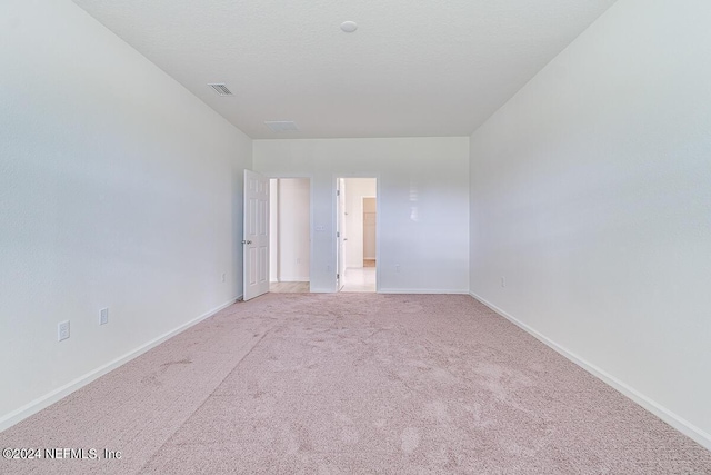 spare room with visible vents, baseboards, a textured ceiling, and light colored carpet