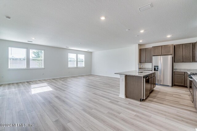 kitchen featuring a center island with sink, light wood-style flooring, appliances with stainless steel finishes, open floor plan, and a sink