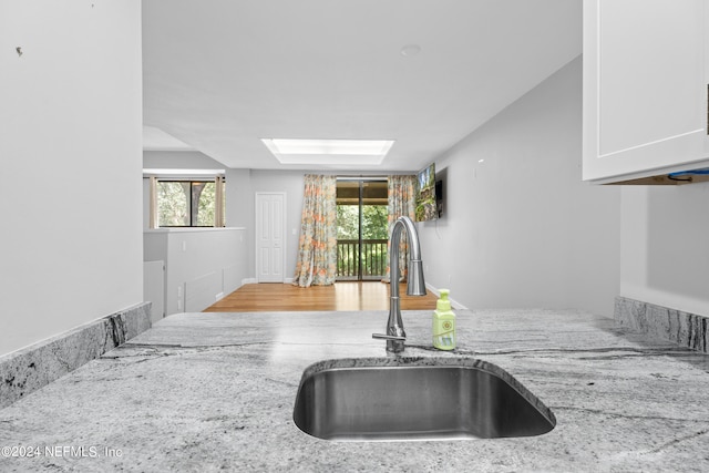 kitchen featuring white cabinets, light stone countertops, sink, and a skylight