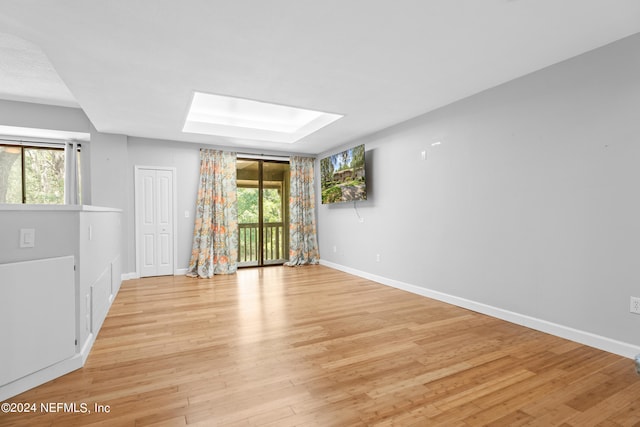 spare room with a skylight, plenty of natural light, and light hardwood / wood-style floors