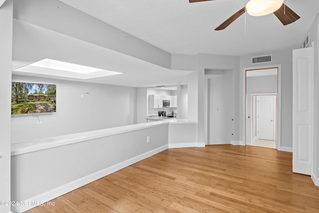 empty room featuring ceiling fan, a skylight, and light hardwood / wood-style flooring