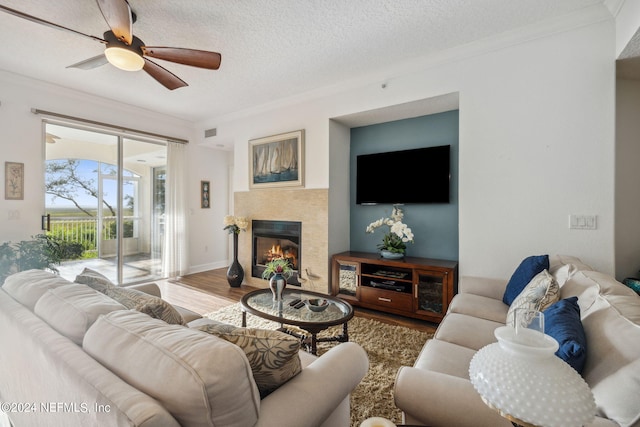 living room with crown molding, wood-type flooring, a textured ceiling, and a tile fireplace