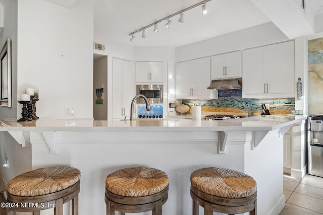 kitchen featuring decorative backsplash, kitchen peninsula, white cabinetry, stainless steel microwave, and a breakfast bar area