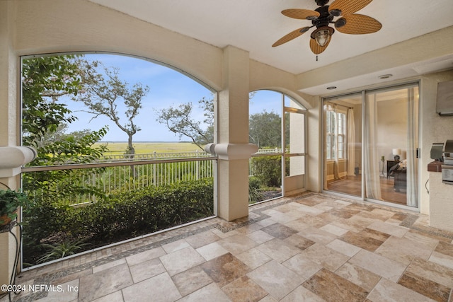 unfurnished sunroom with ceiling fan, a rural view, and a wealth of natural light