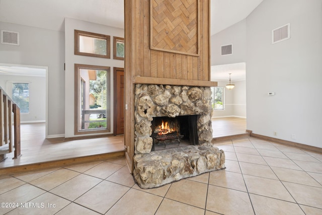 unfurnished living room featuring high vaulted ceiling, a stone fireplace, and tile patterned floors