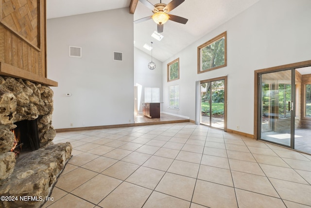 unfurnished living room featuring beam ceiling, a stone fireplace, ceiling fan, and light tile patterned flooring