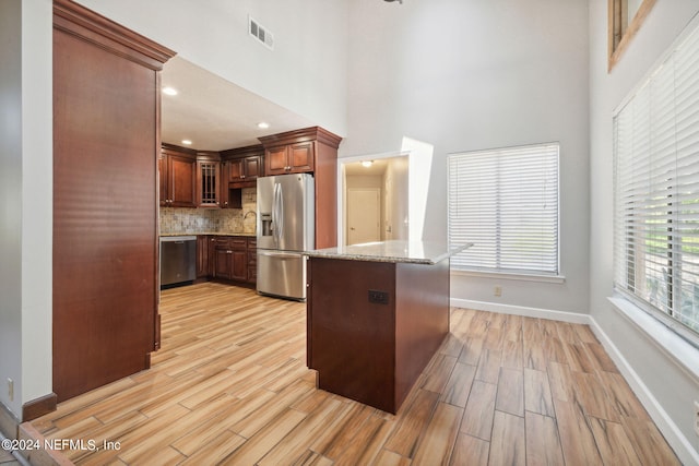 kitchen featuring stainless steel appliances, light stone countertops, backsplash, and light hardwood / wood-style floors