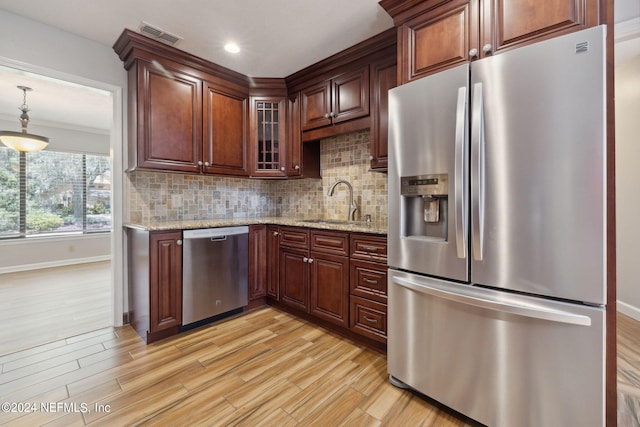 kitchen featuring light hardwood / wood-style flooring, stainless steel appliances, light stone counters, tasteful backsplash, and decorative light fixtures