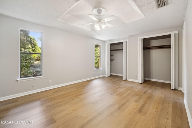 unfurnished bedroom with light wood-type flooring, two closets, and a textured ceiling