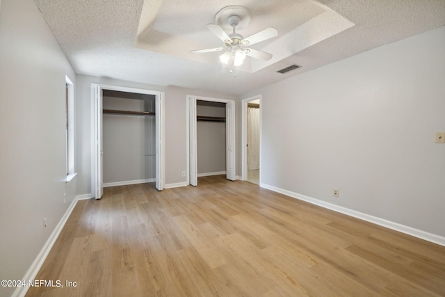 unfurnished bedroom featuring multiple closets, ceiling fan, a textured ceiling, and light wood-type flooring