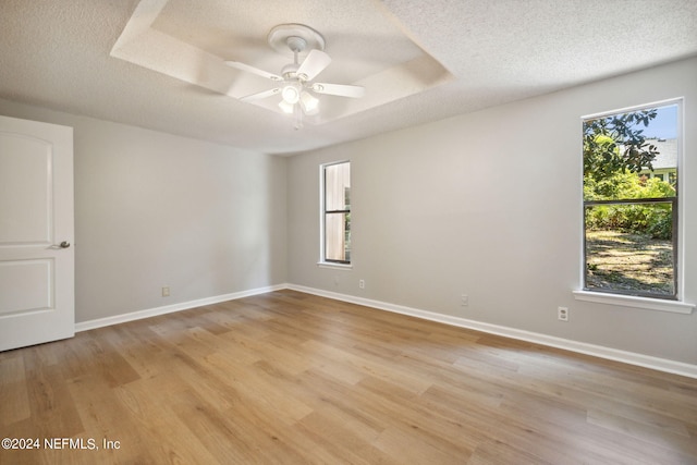 unfurnished room with ceiling fan, a tray ceiling, light hardwood / wood-style floors, and a textured ceiling