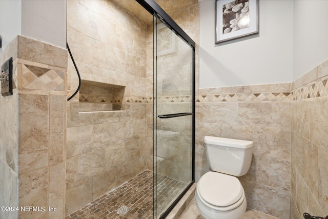 bathroom featuring toilet, a shower with shower door, and tile walls