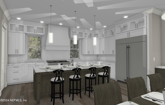 kitchen featuring paneled built in fridge, decorative light fixtures, a kitchen island with sink, and white cabinets