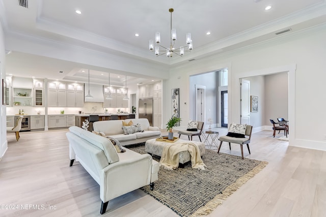 living room featuring a notable chandelier, a raised ceiling, crown molding, and light wood-type flooring