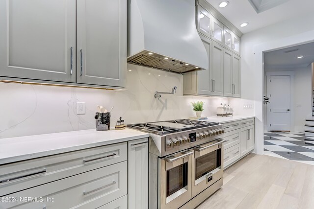 kitchen featuring double oven range, light hardwood / wood-style floors, tasteful backsplash, and custom range hood