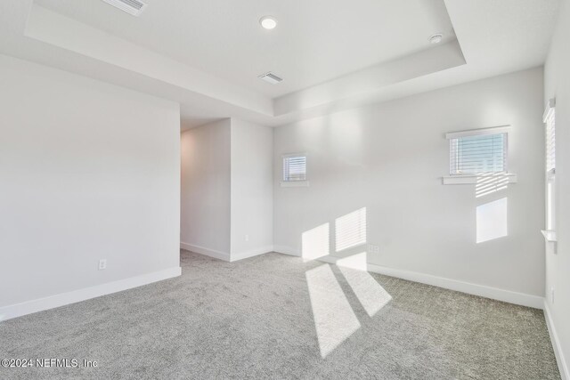 carpeted empty room featuring a tray ceiling