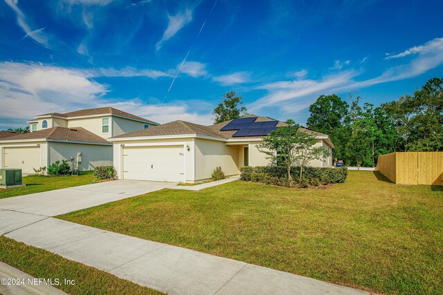 view of front of house with a garage, solar panels, central air condition unit, and a front lawn