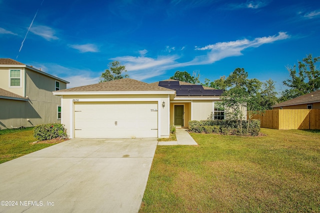 single story home with an attached garage, fence, concrete driveway, roof mounted solar panels, and a front lawn