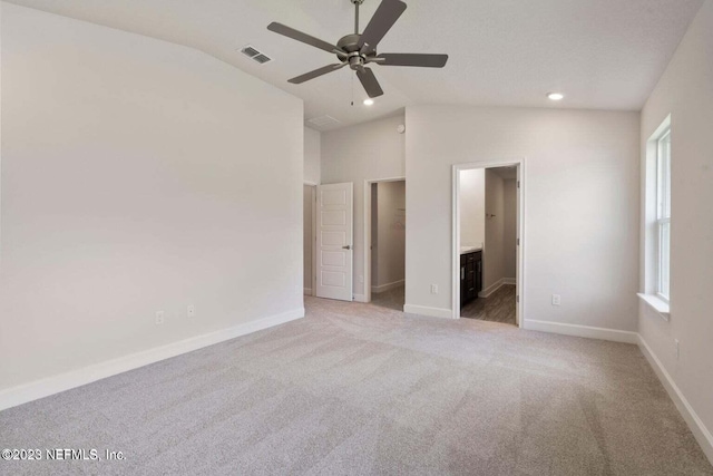 unfurnished bedroom with vaulted ceiling, a spacious closet, ceiling fan, light carpet, and ensuite bath