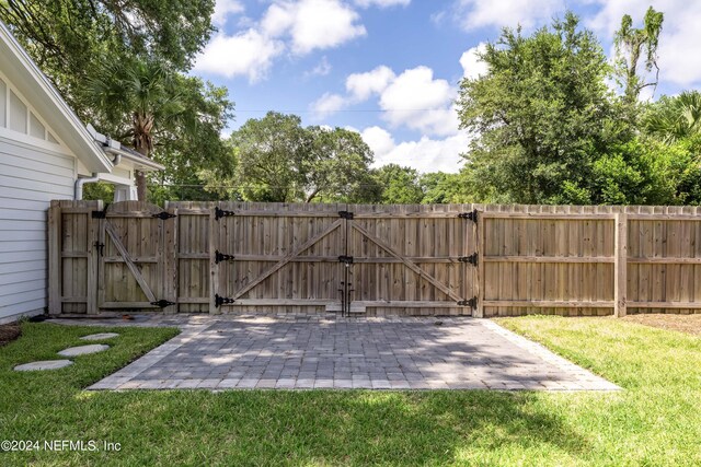 view of gate featuring a lawn and a patio area