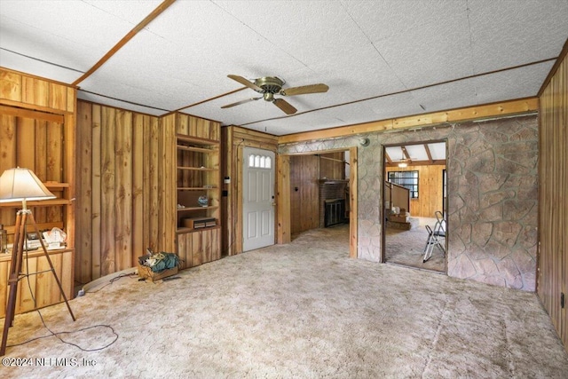 carpeted spare room featuring wooden walls and ceiling fan