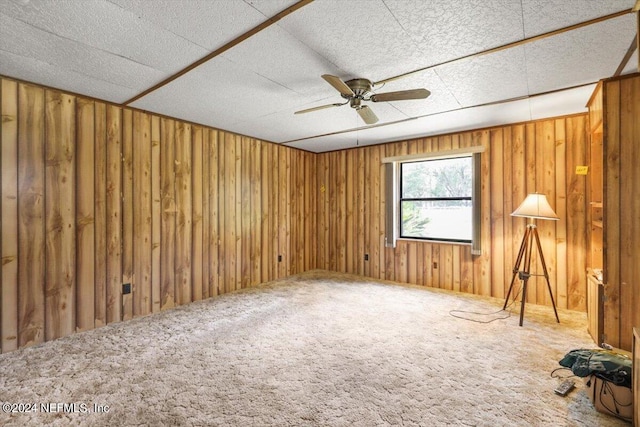 spare room featuring carpet, ceiling fan, and wood walls