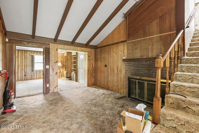 unfurnished living room featuring wooden walls, beam ceiling, carpet floors, and a brick fireplace