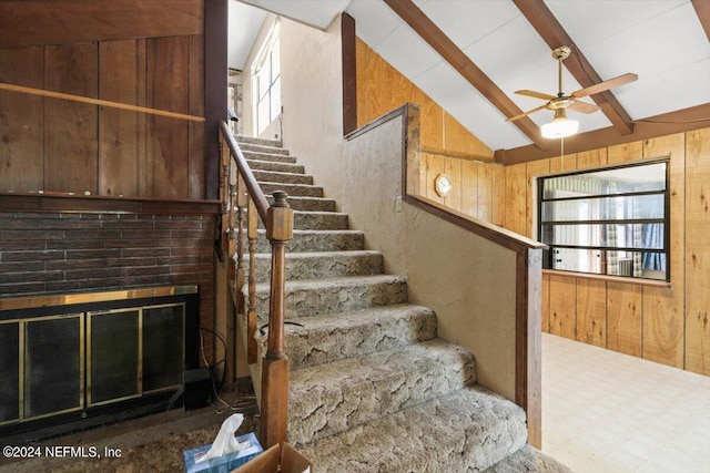 stairway featuring a wealth of natural light, wood walls, ceiling fan, and a fireplace