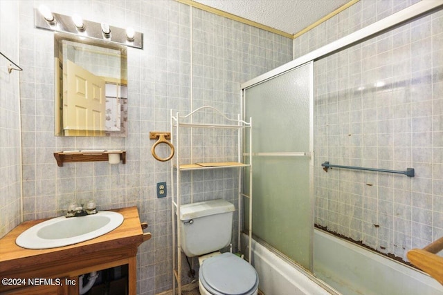 full bathroom featuring shower / bath combination with glass door, tile walls, oversized vanity, toilet, and a textured ceiling