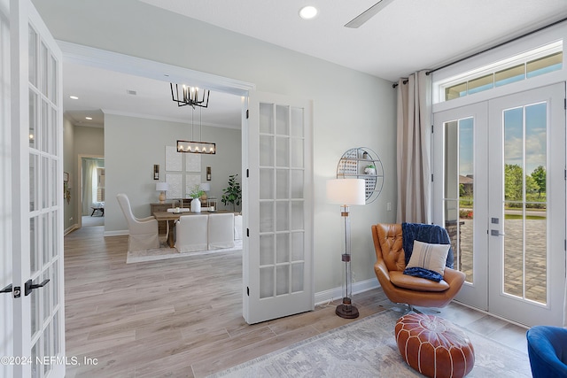 living area with french doors, light wood-type flooring, ornamental molding, and a notable chandelier