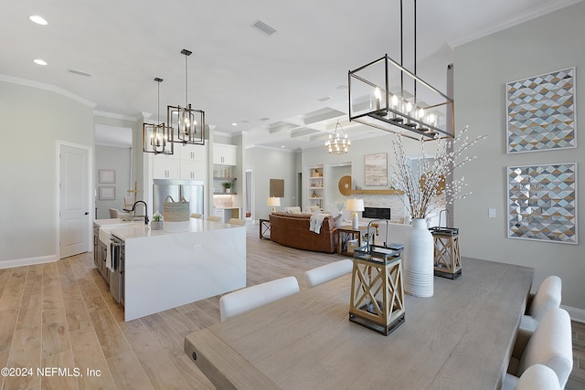 kitchen featuring stainless steel built in fridge, light wood-type flooring, a fireplace, an island with sink, and decorative light fixtures