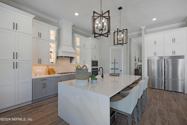 kitchen featuring pendant lighting, a kitchen island with sink, built in appliances, dark hardwood / wood-style flooring, and white cabinetry