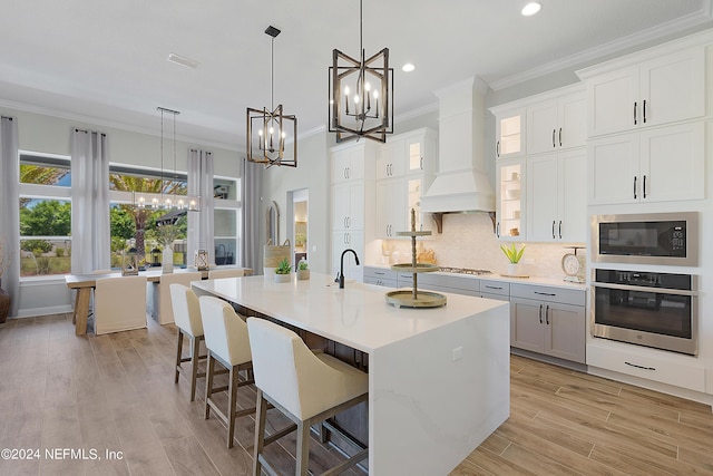 kitchen featuring decorative light fixtures, stainless steel appliances, white cabinetry, and a kitchen island with sink