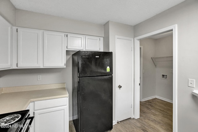 kitchen with black fridge, light wood-type flooring, a textured ceiling, electric range oven, and white cabinetry