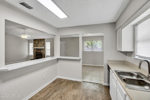 kitchen with white cabinetry, sink, a stone fireplace, a textured ceiling, and hardwood / wood-style flooring