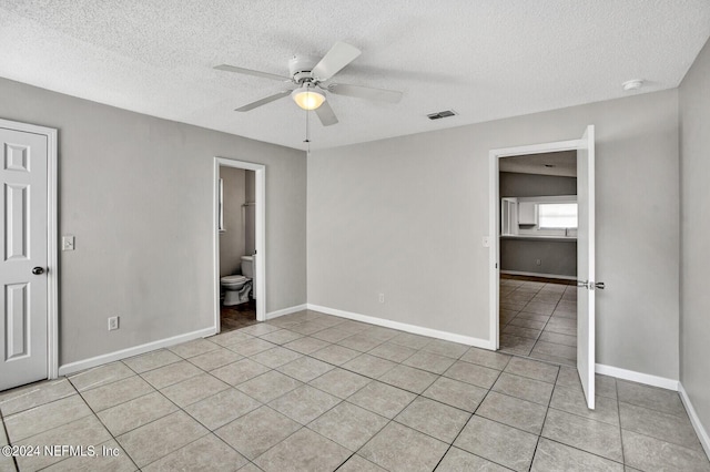 unfurnished bedroom with ensuite bath, ceiling fan, light tile patterned floors, a textured ceiling, and a closet