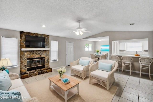 tiled living room featuring a textured ceiling, a stone fireplace, ceiling fan, and lofted ceiling