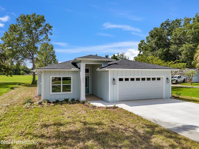 view of front of property featuring a shingled roof, concrete driveway, an attached garage, a front lawn, and board and batten siding