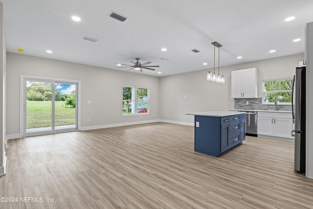 kitchen featuring light wood-style flooring, a kitchen island, appliances with stainless steel finishes, white cabinetry, and backsplash