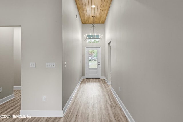 doorway featuring a chandelier, light wood-type flooring, wood ceiling, and baseboards