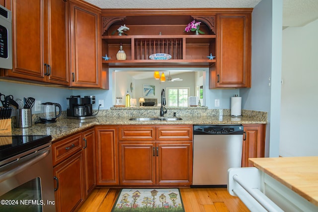 kitchen with dishwasher, sink, ceiling fan, light wood-type flooring, and light stone counters