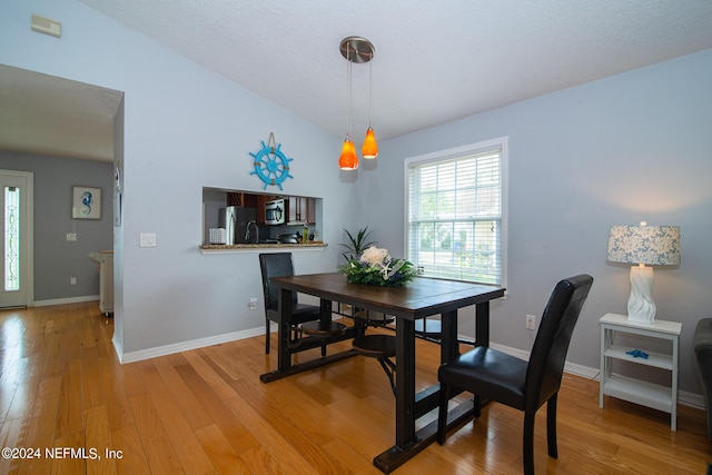 dining area with lofted ceiling, light hardwood / wood-style floors, and a textured ceiling